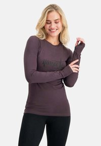 Langärmliges lila Shirt aus weichem Material, mit einem schwarzen, geschwungenen Logo auf der Vorderseite und Daumenlöchern am Bündchen für zusätzlichen Schutz.