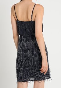 Vestido navy con tirantes finos, que presenta un torso texturizado y un diseño con flecos. La falda tiene un efecto de flecos en capas y en cascada con acentos plateados.