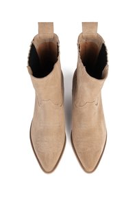 Un par de botines de ante beige con punta afilada y costuras decorativas sobre un fondo blanco, mostrados desde arriba.
