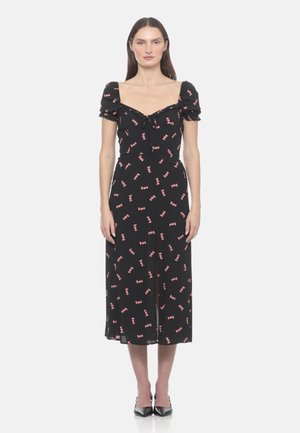 Donna in piedi, indossa un vestito midi nero con stampa di caramelle rosa, maniche a sbuffo, scollo quadrato e tacchi neri appuntiti.