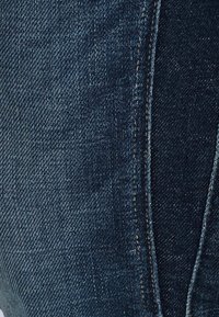 Dark blue denim jeans with a smooth texture, featuring a classic five-pocket design and contrasting stitching along the seams.
