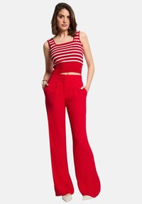 Pantalones anchos rojos de cintura alta, combinados con un top corto a rayas rojas y blancas. El tejido parece suave, con bolsillos en los pantalones.