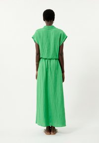 Green linen maxi dress with short sleeves and a collared neck, featuring a cinched waist and a flowing, textured design.
