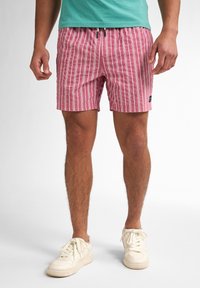 Costumi da bagno a righe rosse e bianche realizzati in tessuto leggero. Presentano un elastico in vita con cordino e una patch con il logo sul lato.