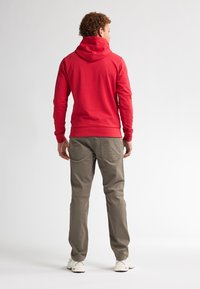Hanorac roșu cu guler înalt și manșete ajustate, asortat cu pantaloni cargo gri deschis. Ținuta are un design casual și detalii vizibile de cusătură.