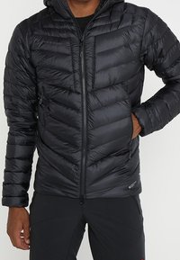 Černá, nadýchaná zateplená bunda s kapucí, která má vzor v chevronovém prošívání, plný zip v přední části a elastické manžety. Lehký materiál.