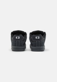 Black athletic shoes with a smooth upper, padded collar, and textured sole. Notable white stitching and logos on the heel and side.