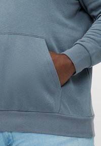 Hooded sweatshirt in soft, light teal fabric. Features a front pocket, ribbed cuffs, and hem. Smooth texture with minimal seams.