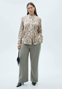 Langsluig blouse in een beige slangenprint, gecombineerd met lichtgrijze broek met wijde pijpen. Accessoires omvatten een kleine zwarte handtas.