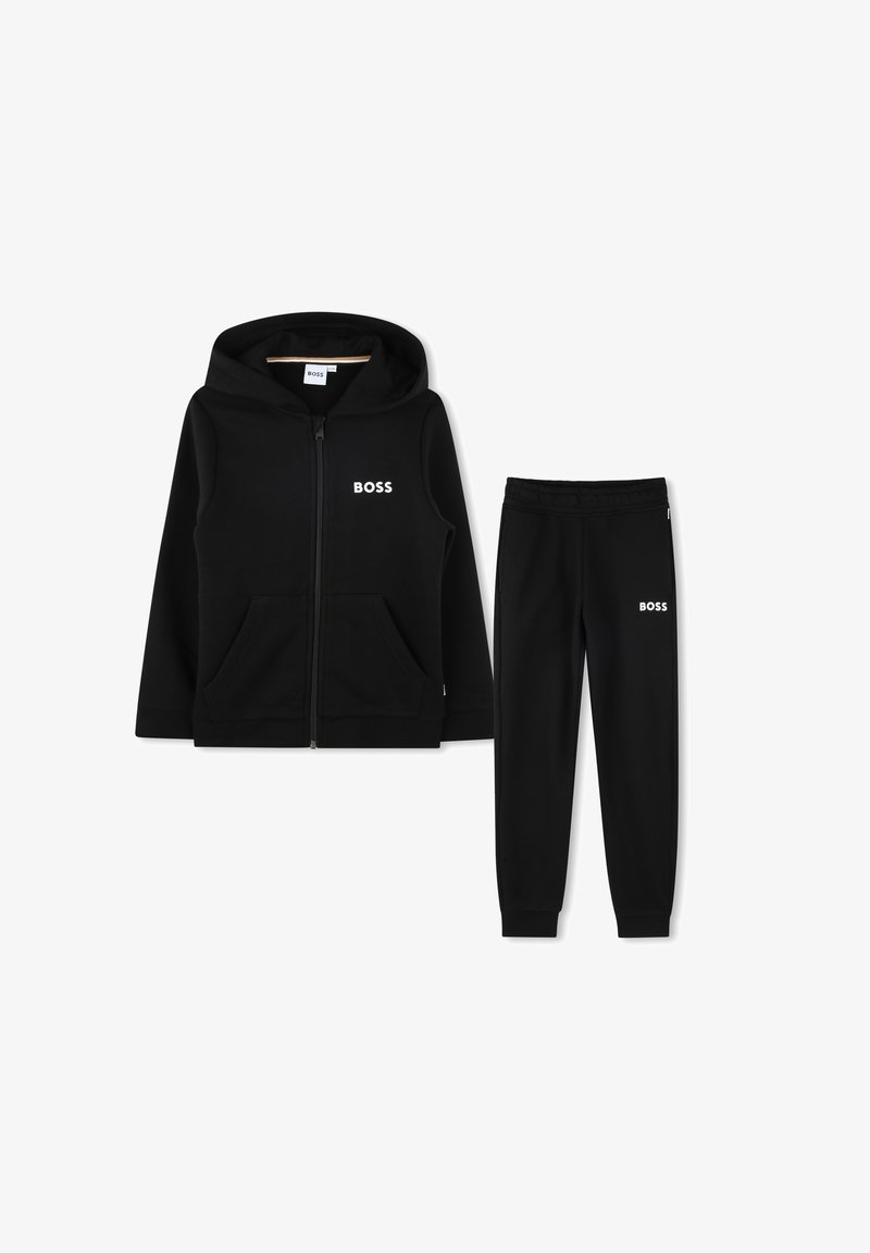 Felpa nera con zip e pantaloni tuta coordinati, con logo bianco "BOSS" sul petto e sulla coscia, posati su uno sfondo bianco.
