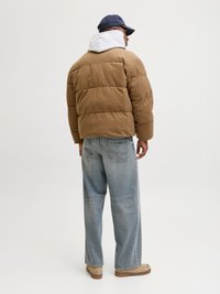 Brun cordfløyel pufferjakke med grå hette, kombinert med lyseblå baggy jeans og beige fottøy. Capsen har en mørk blå farge.