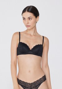 Sosten negro de encaje con bordes en forma de ondas, con un diseño acolchado y tirantes ajustables. Combinado con braguitas de encaje a juego.