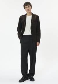 Bruine suede blazer over een wit T-shirt, gecombineerd met zwarte wijde broek en zwarte schoenen. Eenvoudig ontwerp, gladde textuur en neutrale kleuren.