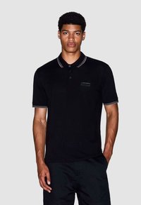 Zwarte polo shirt met een kraag, voorzien van grijs gestreepte accenten en een klein logo op de linkerborst. Gemaakt van zacht, glad stof.