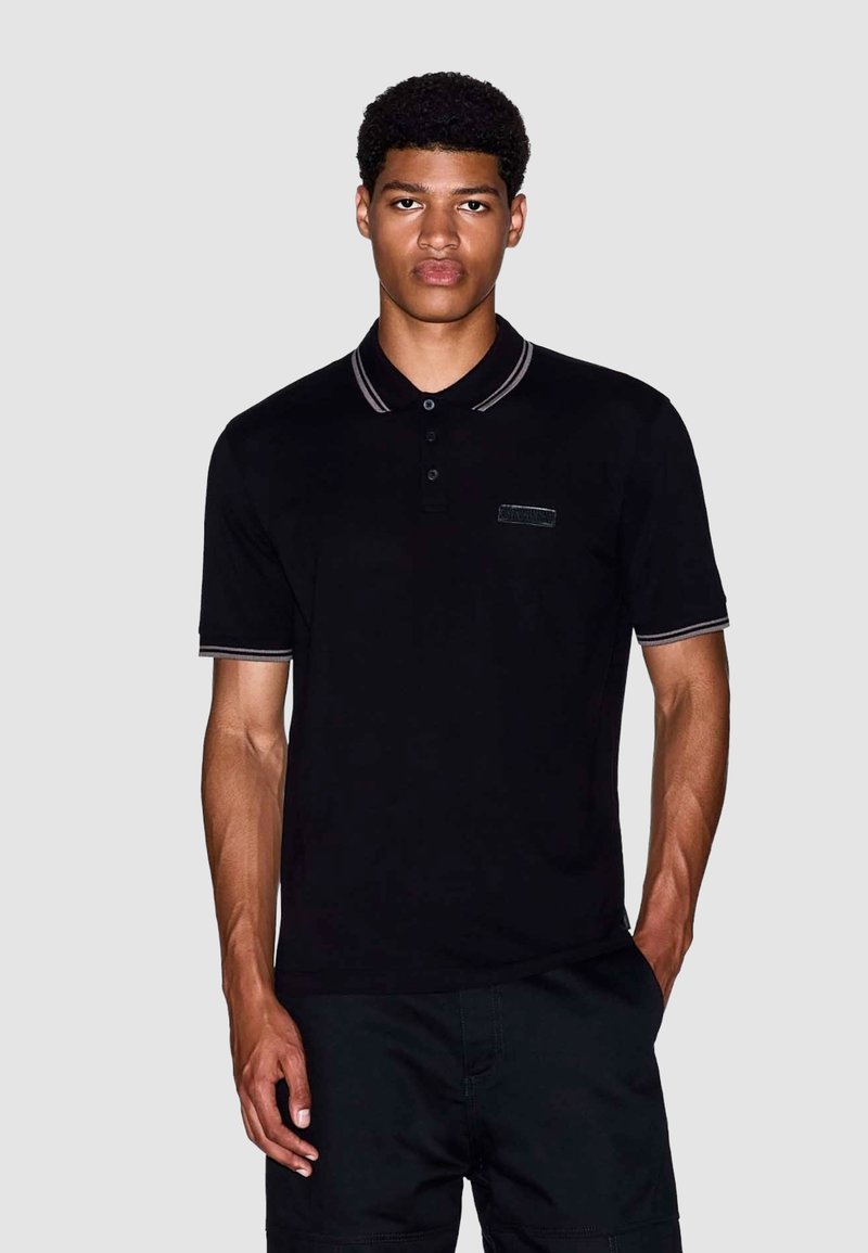 Zwarte polo shirt met een kraag, voorzien van grijs gestreepte accenten en een klein logo op de linkerborst. Gemaakt van zacht, glad stof.