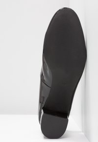 Semelle d'une chaussure de ville noire cirée à petit talon, taille 37, positionnée verticalement contre une surface blanche.