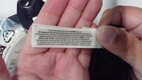 Mains tenant une étiquette d'entretien de vêtement indiquant la composition du tissu et les instructions de lavage en plusieurs langues.