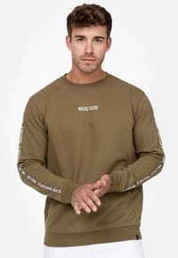 Olive green sweatshirt made of a soft fabric. Features long sleeves, round neckline, and white branding text on the chest and sleeves.