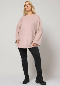 Un pull surdimensionné texturé rose clair à manches longues, associé à un pantalon noir ajusté et des bottines noires à talons épais.