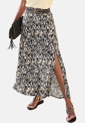 Woman wearing leopard print maxi skirt with side slit, black belt, holding black woven clutch, and black sandals with gold discs.