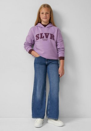 Sweat à capuche violet avec le texte "SLVR", associé à un jean bleu évasé et des baskets blanches. Tissu doux et coupe décontractée.