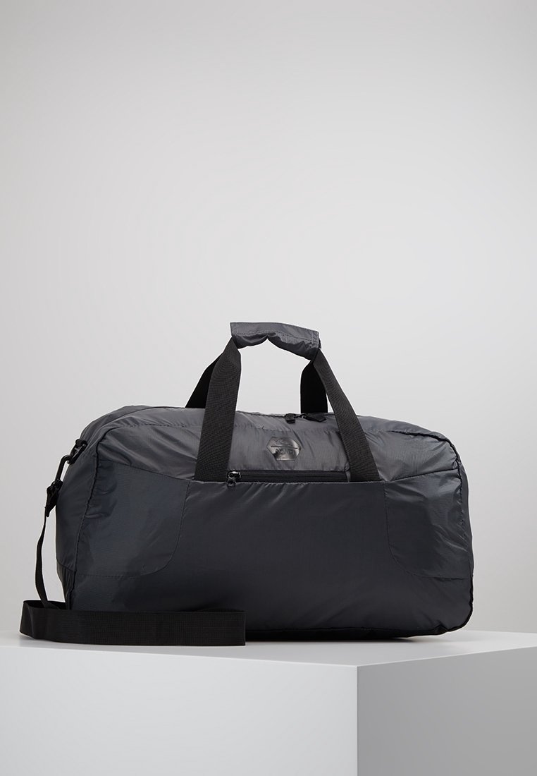 Musta pehmeä duffel-laukku, jossa on kaksi kantokahvaa, etupuolella vetoketjullinen tasku ja säädettävä olkahihna valkoisella alustalla.