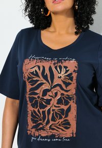 Camiseta de marina de manga corta con un diseño floral en color cobre, fondo texturizado salpicado y texto blanco que dice "La felicidad es hacer realidad tus sueños."