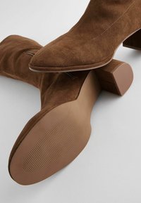 Stivaletti in suede marrone con punta appuntita, tacco quadrato rettangolare e suola in gomma liscia caratterizzata da leggere linee di texture.