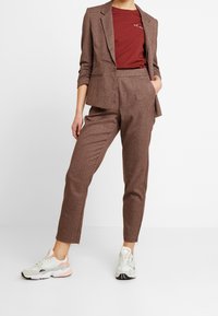 Brun rutet jakkesæt med en tætsiddende blazer og højlivet bukser, parret med lyse sneakers med rosa og grå detaljer.