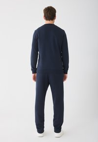 Marineblauwe sweatshirt en bijpassende joggers gemaakt van zachte stof; heeft ribgebreide manchetten en zoom, een gladde textuur en een relaxte pasvorm.