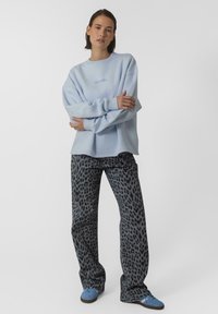 Jasnoniebieski, luźny sweatshirt z okrągłym dekoltem, w zestawie z czarnymi spodniami w szary wzór lamparta. Niebieskie sneakersy dopełniają całość.