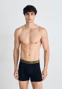 Schwarze Boxer-Briefs mit einem goldenen "HUGO"-Bund, aus weicher Baumwolle gefertigt, mit einer engen Passform und einem Design bis zur Mitte des Oberschenkels.