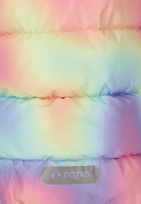 Vadderad jacka i pastellregnbågsgradient. Har kviltad textur och en silverfärgad "ZIGZAG"-logotyp på den nedre delen.