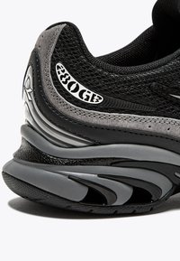 Sneaker nero e grigio con tomaia in rete, dettagli texturizzati, design elegante e un logo prominente di lato. Suola in gomma ammortizzata.