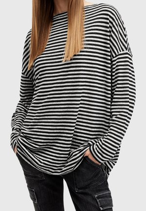 Camicia a maniche lunghe a righe bianche e nere con vestibilità ampia, scollo rotondo e spalle cadenti, abbinata a pantaloni cargo scuri.