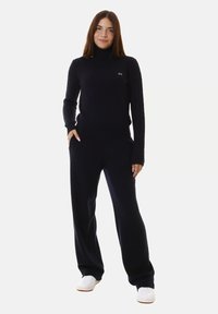 Maglione a collo alto a coste in blu navy abbinato a pantaloni a gamba larga coordinati. Presenta maniche lunghe e un piccolo logo sul petto.