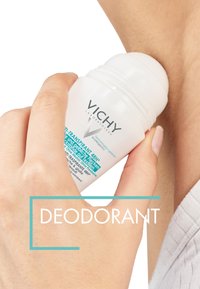 White roll-on deodorant with blue labeling held against a skin tone background, featuring a smooth top and clear branding details.