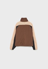 Veste en blocs de couleurs marron, noir et beige avec manches longues et col montant, vue de dos sur un fond uni.