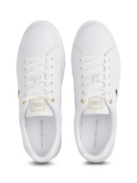 Valge nahast sneakers, millel on paelad, tekstuursed küljed, kullavärvi detailid ja tugevdus varbale. Bränding on nähtav keeles ja sisetallal.