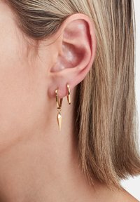 Gouden hoepeloorbellen met een hangende puntvormige charme. Het ontwerp heeft een gepolijste afwerking en een geometrische vorm, wat een moderne esthetiek benadrukt.