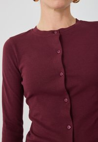 Burgundský cardigan s dlouhým rukávem, hladká tkanina, kulatý výstřih, s pěti ladícími knoflíky vpředu. Jednoduchý, přiléhavý design.