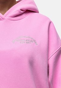 Felpa rosa realizzata in tessuto morbido, dotata di cappuccio e con un logo ricamato che recita "GOOD FOR NOTHING BRITISH ATELIER EST 2011."