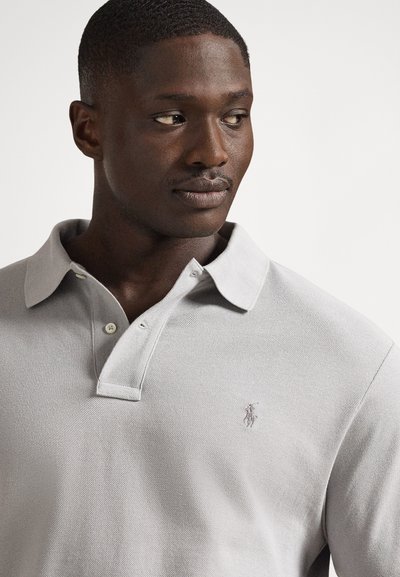 Ανοιχτό γκρι πόλο μπλούζα από υφή υφάσματος, με κλασικό γιακά, τρία κουμπιά και διακριτικό κεντημένο λογότυπο στο αριστερό στήθος.