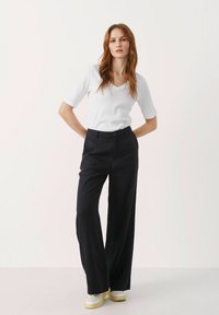 Weißes V-Ausschnitt-T-Shirt kombiniert mit weit geschnittenen navyblauen Hosen. Auffällige Details sind ein Knopfverschluss und elegante Sneakers mit gelber Sohle.