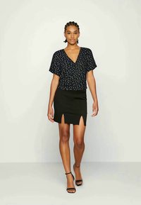 Top preto de manga curta com um padrão floral, combinado com uma saia preta com uma fenda frontal. A modelo usa sandálias pretas.