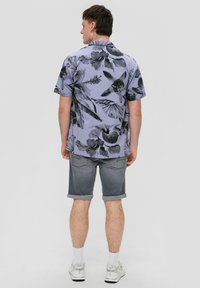 Koszula z krótkim rękawem w jasnofioletowym kolorze z czarnym wzorem liści; połączona z szarymi szortami z podwiniętymi nogawkami. Widać białe skarpetki i białe buty.