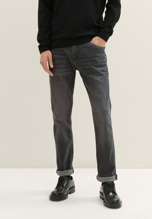 Donkergrijze denim jeans met een recht model, voorzien van opgerolde manchetten, vijf zakken en versleten details, gecombineerd met zwarte leren schoenen.
