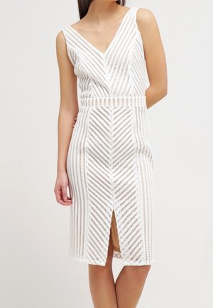 Abito bianco senza maniche fino al ginocchio con motivo a spina di pesce in pizzo, scollo a V, vita aderente e spacco frontale, indossato da una donna in piedi.