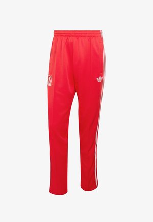 Červené tepláky značky Adidas s bílými pruhy na stranách, elastickým pasem a logem Liverpool FC na levém stehně.