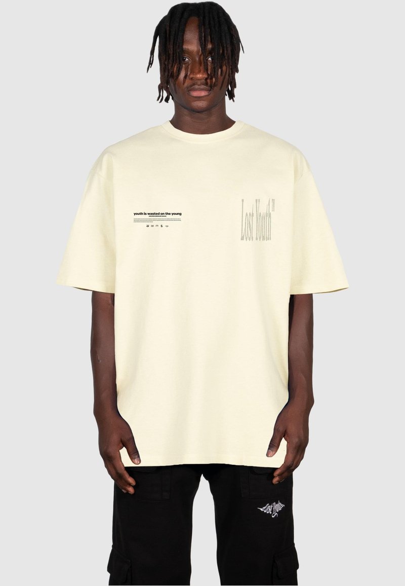 T-shirt a maniche corte di cotone giallo chiaro con elementi grafici di testo; "Gioventù Perduta" stampato in grande font a destra e una frase più piccola a sinistra.